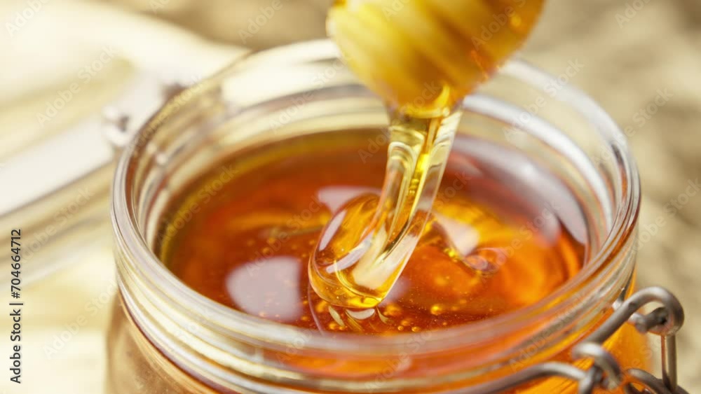 Honey dripping from wooden dipper. Healthy food concept. Honey in glass jar. Honey dripping from wooden honey spoon. Close-up in 4K, UHD