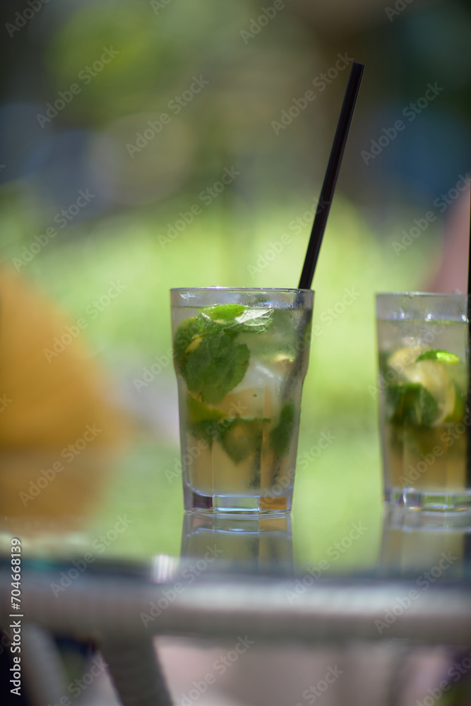 Refreshing green lemonade in a glass on the table against the background of nature. Freshly squeezed drinks with ice. Lemonade with lemon, mint lime and herbs