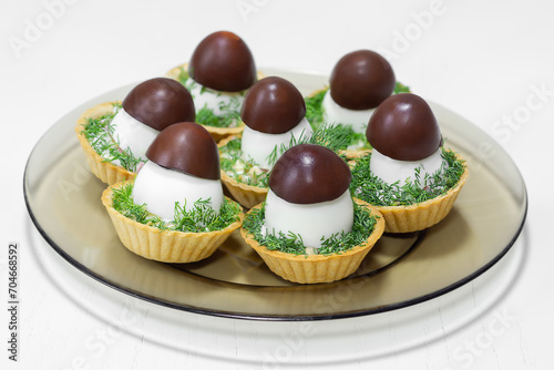 A festive snack in tartlets with salad decorated with a mushroom-shaped egg on a white wooden background. Selective focus