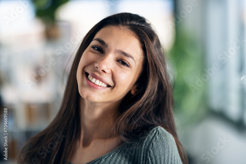 Smiling young woman posing while looking at camera in the living room at home.