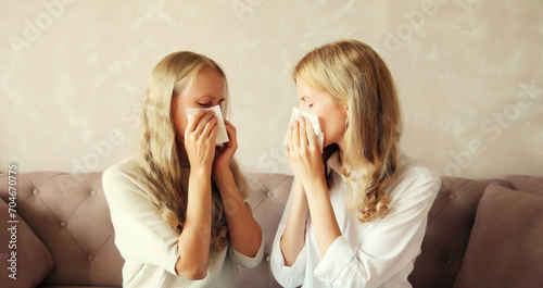 Sick exhausted middle-aged woman mother and adult daughter together sneezing blow nose using tissue at home