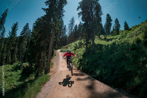 Downhill mountain biking on a shaped bike park trail in Austria, sunny blue sky day, jumping between trees.