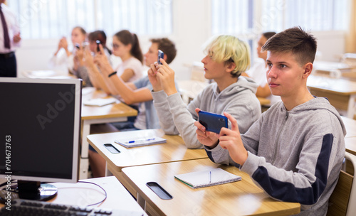 Teen students using smartphones to find necessary information on lecture in college class © JackF