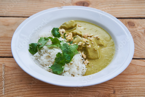 Close up picture of deep rustic porcelain plate with sweet and spicy indian style green lamb curry sprinkled with roasted cashew nuts and served with fresh coriander leaves on the white basmati rice.
