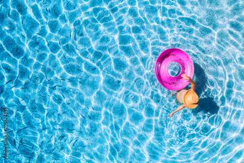 Aerial view of a young woman in hat swimming with pink swim ring in blue sea with school of fish at sunset in summer. Tropical landscape with girl, clear water, sandy beach in Greece. Top view. Travel