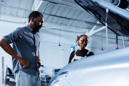 Mechanic at auto repair shop conducts annual vehicle checkup, informing customer about needed steering mechanism replacement. Competent garage worker talks with customer after finishing car inspection © DC Studio