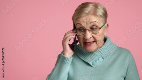 Aged well-groomed blonde short-haired impulsive lady in spectacles blue sweater, having an unpleasant conversation on cell phone, nervously waving her hand. High quality 4k footage photo