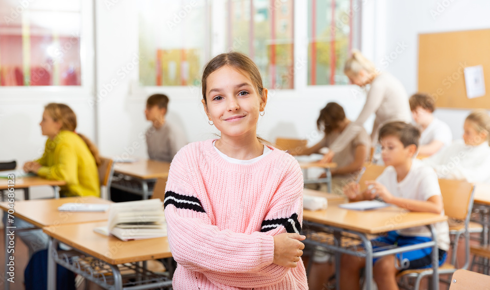 Portrait of smiling positive schoolgirl posing in classroom during lesson in secondary school - obrazy, fototapety, plakaty 
