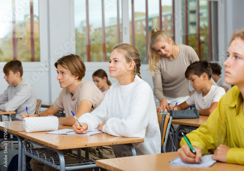 Group of diligent school kids and teacher during lesson in classroom in secondary school