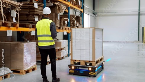 Warehouse worker manipulating with an industrial robot in modern industrial warehouse.
