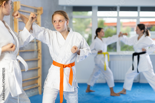 Concentrated adolescent girl in kimono honing punching techniques during kumite at karate training session