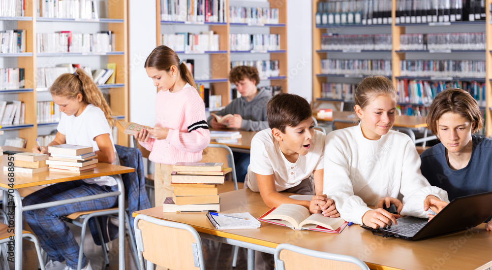 © JackF - Three schoolchildren preparing for lessons in the school library are looking for the necessary information on a laptop, ..discussing topical issues