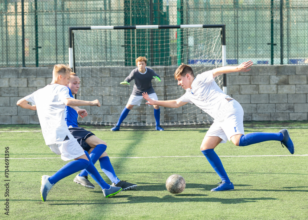Fototapeta premium Game moments of football match between two teams of teenagers in white and blue shirts