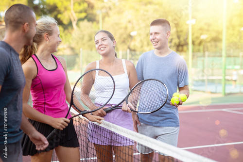 Group photo of positive people standing on tennis court after another game and having conversation.