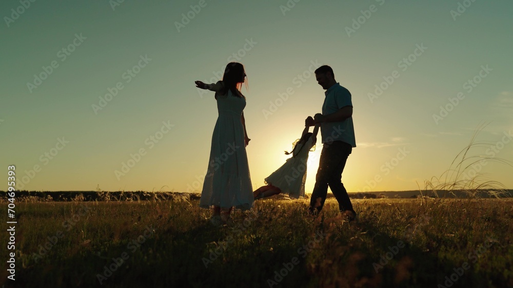 Family playing and nature at sunset. Playful family time with mother twisting daughter in arms and handing over girl to father on field. Happy parents with child creating memories of sunset moments