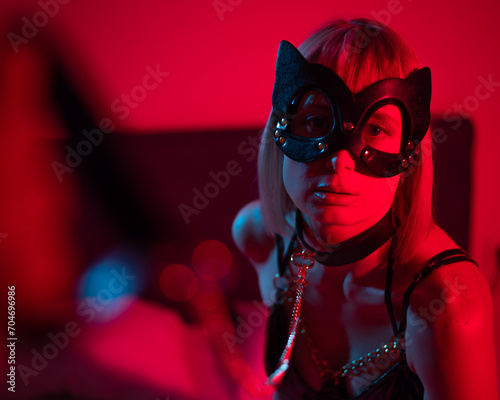 Blonde girl in a leather mask and handcuffs in the bedroom in red blue neon light. Role-playing games. photo