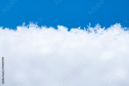Snowy surface with empty blue and white space for text. Crystal snowflakes on white snow close-up. Winter macro background.