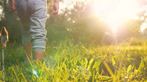 Little contented child joyfully dashes barefoot on grass in park during warm weather. In meadow gleeful child boy sprints shoeless across lush greenery. Happy kid runs cheerfully across grass photo
