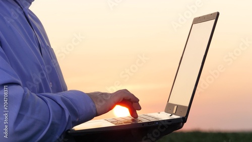 Agriculturist uses keyboard on laptop on corn field closeup. Skilled farmer cultivates corn using computer technology on rural land. Agronomist stores data on laptop while inspecting corn field