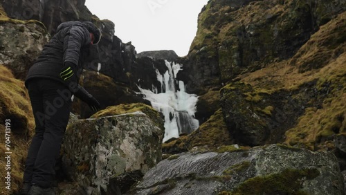 Man climb volcanic rock to reach sightseeing area near Icelandic waterfall photo