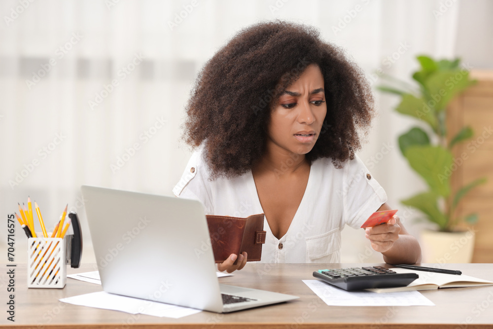 Confused woman with credit card and wallet planning budget at table in room. Debt problem Confused woman with credit card and wallet planning budget at table in room. Debt problem