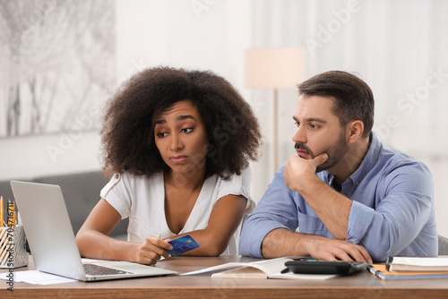 Confused couple with credit card using laptop for planning budget at home. Debt problem