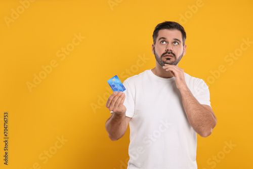 Confused man with credit card on orange background, space for text. Debt problem © New Africa