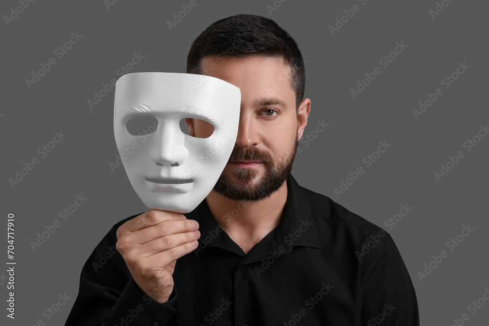 Multiple personality concept. Man covering face with mask on grey background Multiple personality concept. Man covering face with mask on grey background