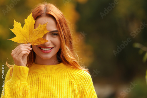 Smiling woman covering eye with autumn leaf outdoors. Space for text