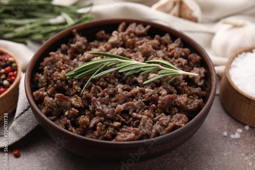 Fried ground meat in bowl and rosemary on brown textured table, closeup