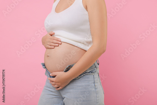 Pregnant woman in jeans on pink background, closeup © New Africa