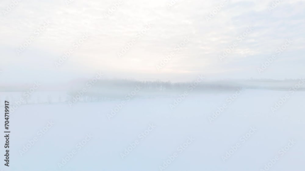 Moving through fog and ascending to reveal a vast nordic scandinavian landscape with forest covered in snow and ice and fog engulfing the beatiful scenery. Car is driving on a road. Tammela, Finland.