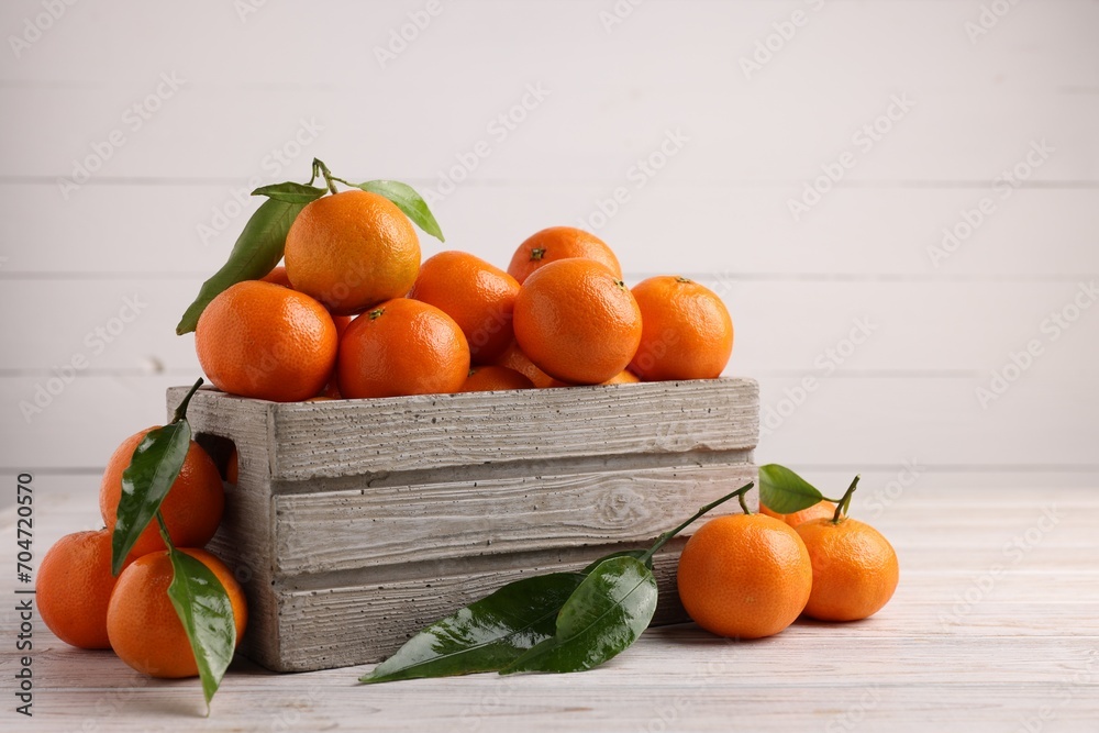 Delicious tangerines with leaves on light wooden table. Space for text