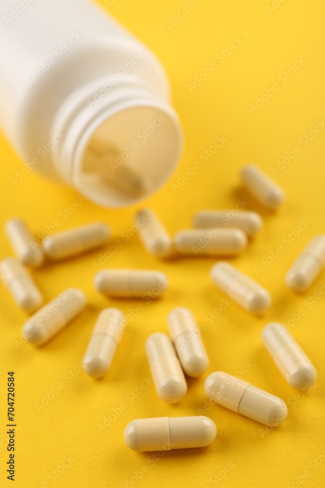 Bottle and vitamin capsules on yellow background, closeup Bottle and vitamin capsules on yellow background, closeup