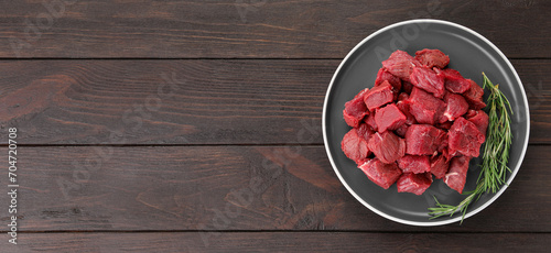 Pieces of raw beef meat with rosemary on wooden table, top view. Banner design with space for text