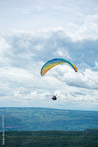 A person paragliding in the sky with a colorful parachute and safety harness.Mountains, Extreme sports in a cloudy day 