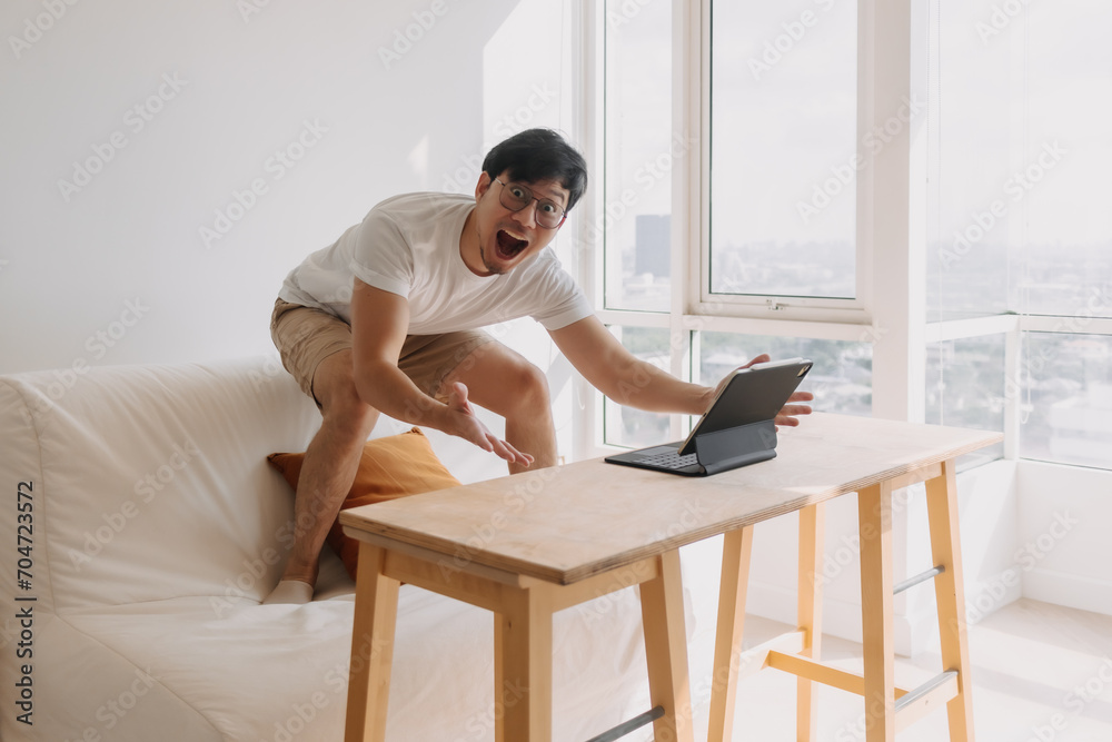 Funny Asian man overly happy and excited with his work success and victory in the computer tablet. Funny Asian man overly happy and excited with his work success and victory in the computer tablet.
