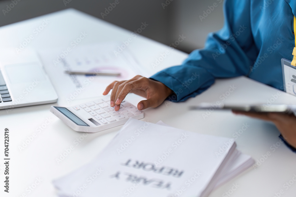 Businesswoman using a calculator to calculate numbers on a company's financial documents, she is analyzing historical financial data to plan how to grow the company. Financial concept Businesswoman using a calculator to calculate numbers on a company's financial documents, she is analyzing historical financial data to plan how to grow the company. Financial concept