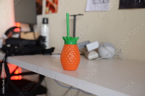 Copo de abacaxi laranja com canudo verde, utensilio de cozinha exótico em cima da bancada  photo