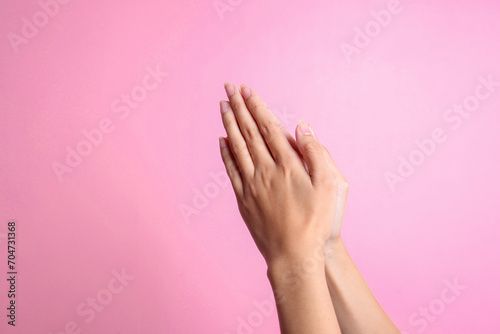 Female hands showing praying gesture against pink background.  photo