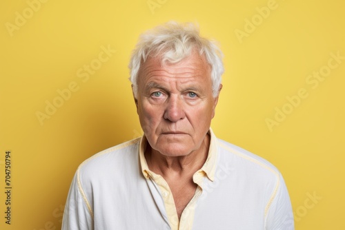 Portrait of a sad senior man looking at camera over yellow background