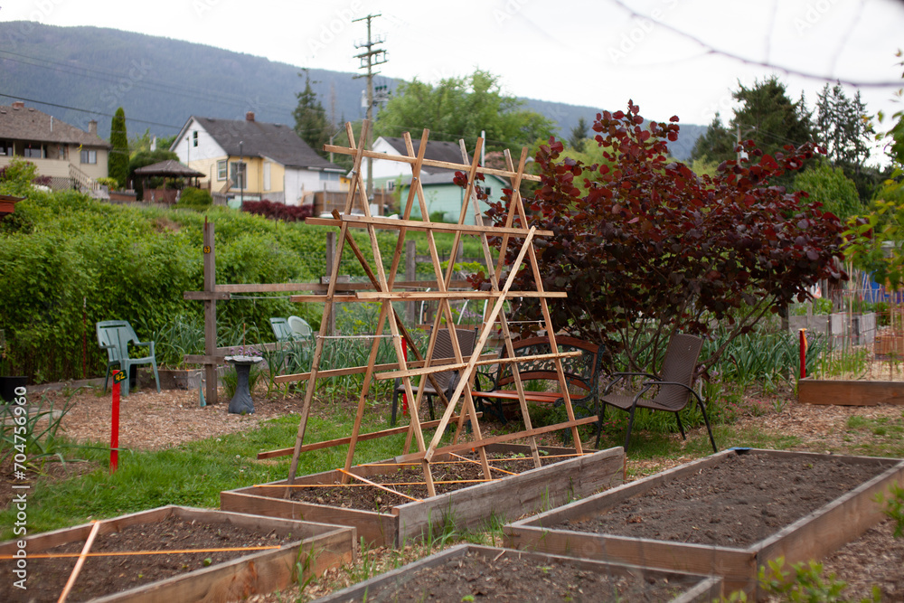 A large, wooden A-Frame trellis sits on top of a raised garden bed in a community garden. Cucumbers, tomatoes and other vining plants really benefit from growing up a trellis.