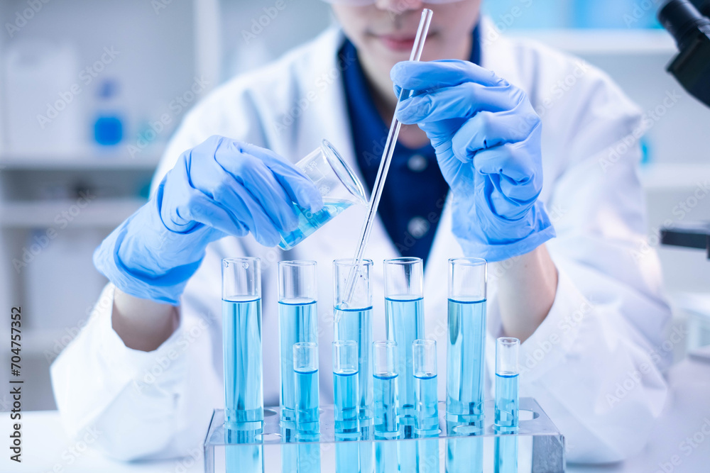 Woman research scientist biology chemistry medicine pouring liquid from beaker to test tube indoor science laboratory room, adult female person blue glove work discovery experiment medical chemist Woman research scientist biology chemistry medicine pouring liquid from beaker to test tube indoor science laboratory room, adult female person blue glove work discovery experiment medical chemist