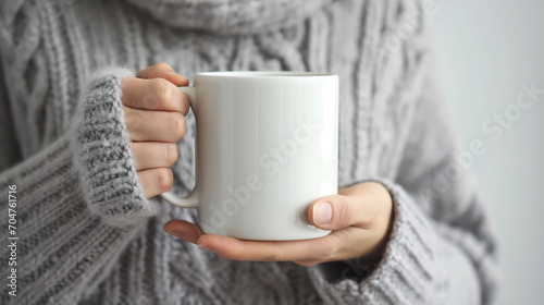 Womans hands in grey sweater holding a white coffee mug.
