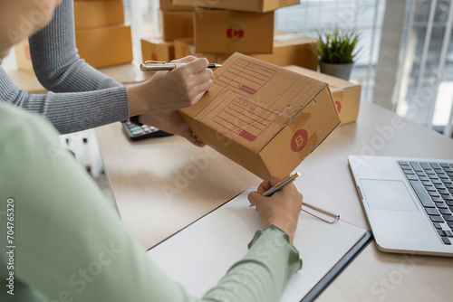 Young business woman working online e-commerce shopping at home. Young woman seller prepare parcel box of product for deliver to customer photo