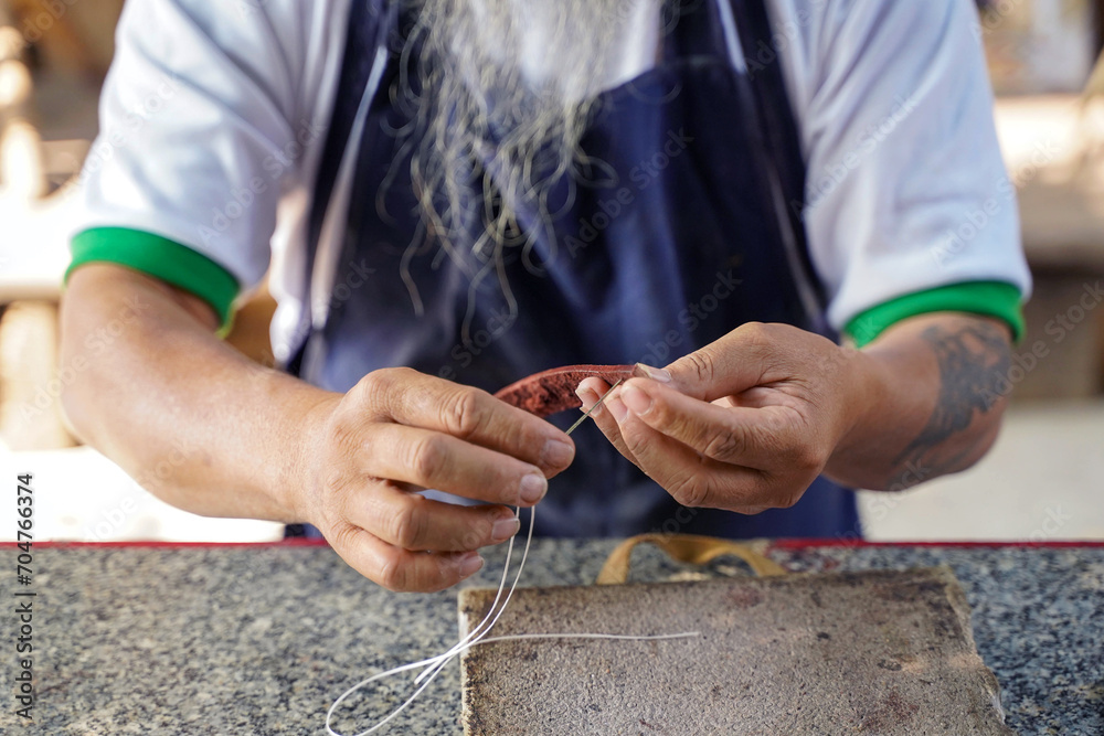Closeup hands of Asian leather craftsman is carefully to sew a leather belt for a customer., Leather craftsman concept.