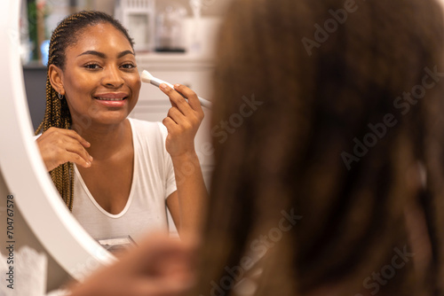 Smiling of african american woman clean healthy skin looking at mirror.beauty and fashion,hair,black skin,skin care,cosmetics,cosmetology,african girl apply cream moisturizer on face.spa and wellness photo