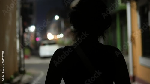 Unrecognizable young girl with solitude walking alone on a dimly lit street at night. photo