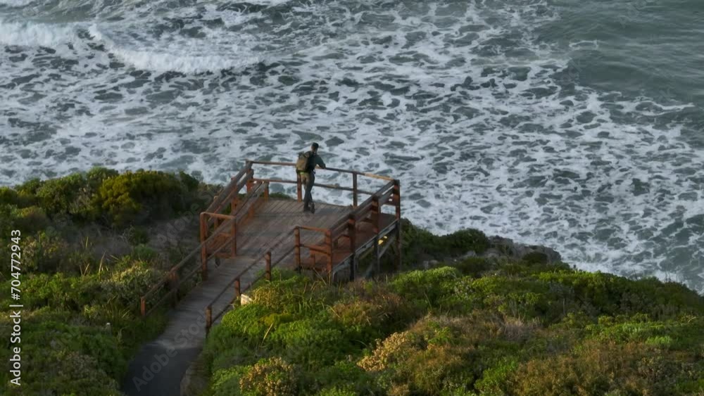 Parallax shot, descending and tilting up as a man looks out over the beach from the nearby cliffs. Parallax shot, descending and tilting up as a man looks out over the beach from the nearby cliffs.