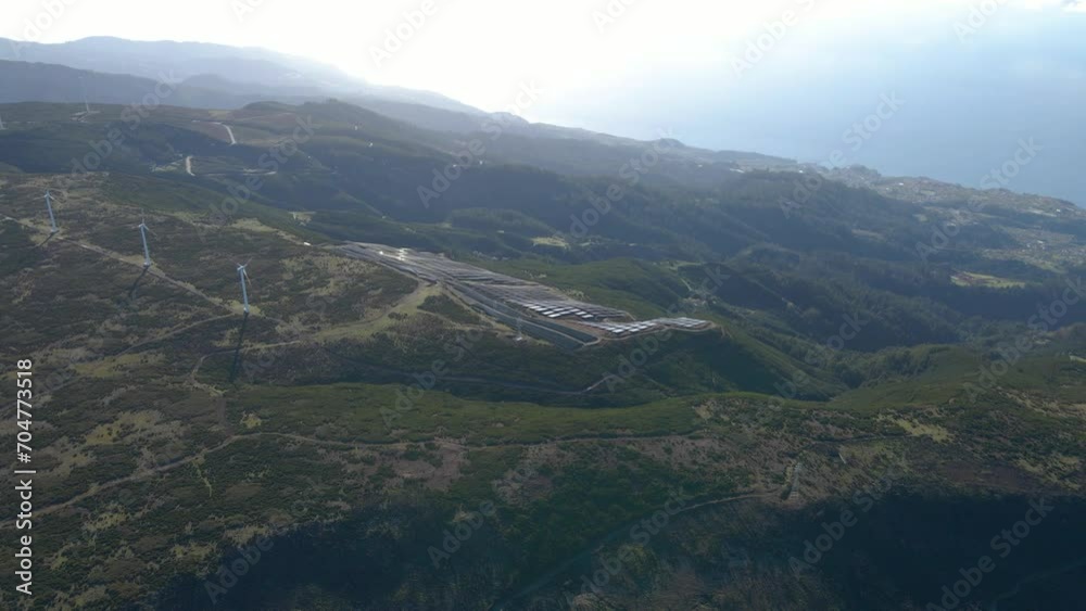 Aerial view of a photovoltaic farm and a wind farm on top of a mountain in Paul da Serra Madeira island. Drone moving forward in direction to the panels, blue sky in the background, 4K, 60 fps. Aerial view of a photovoltaic farm and a wind farm on top of a mountain in Paul da Serra Madeira island. Drone moving forward in direction to the panels, blue sky in the background, 4K, 60 fps.